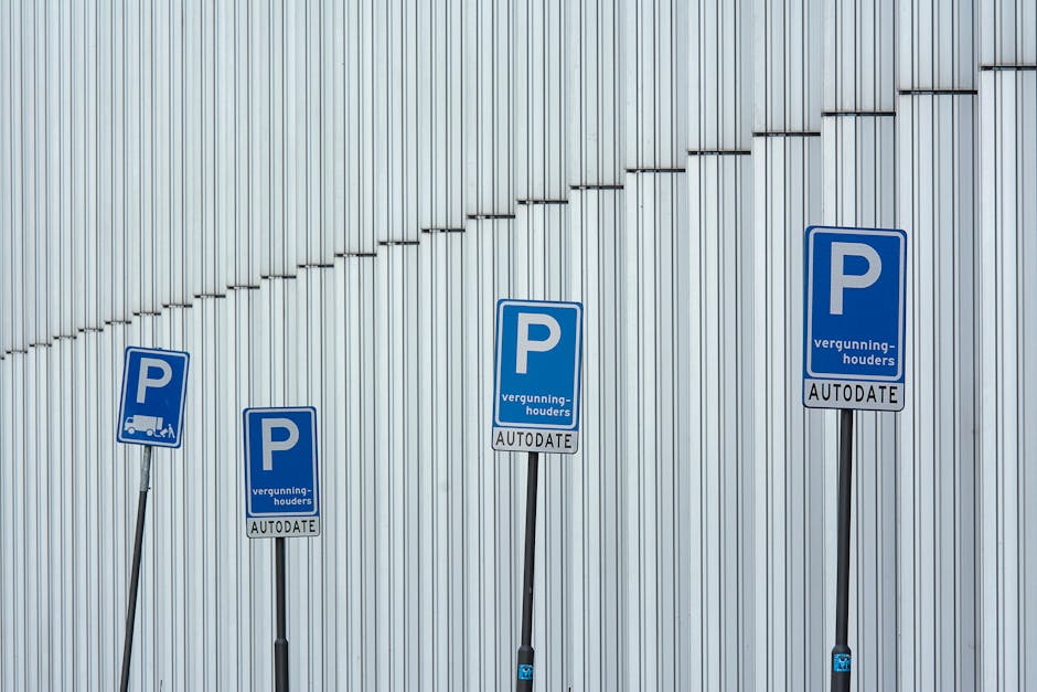 Two blue industrial garage doors are situated within a brick building, with each door featuring small rectangular windows near the top. In front of the doors, a paved loading area is visible, with thr